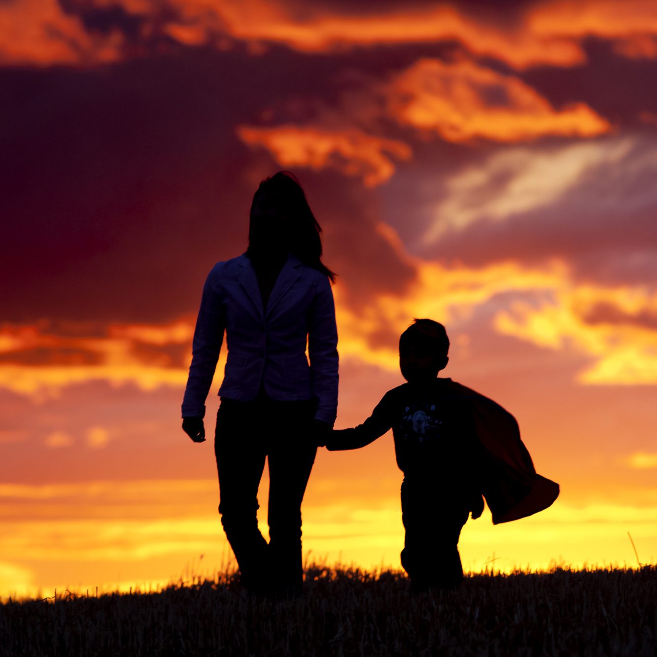 A tender moment of a mom and her son walking along at sunset.